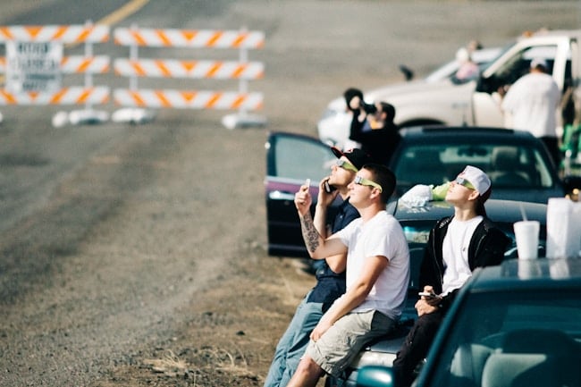 Jovenes en sus coches y sus gafas de sol esperando el momento idóneo para ver el eclipse solar